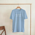 Light blue t-shirt with a dog graphic and text on a wooden hanger against a beige wall.