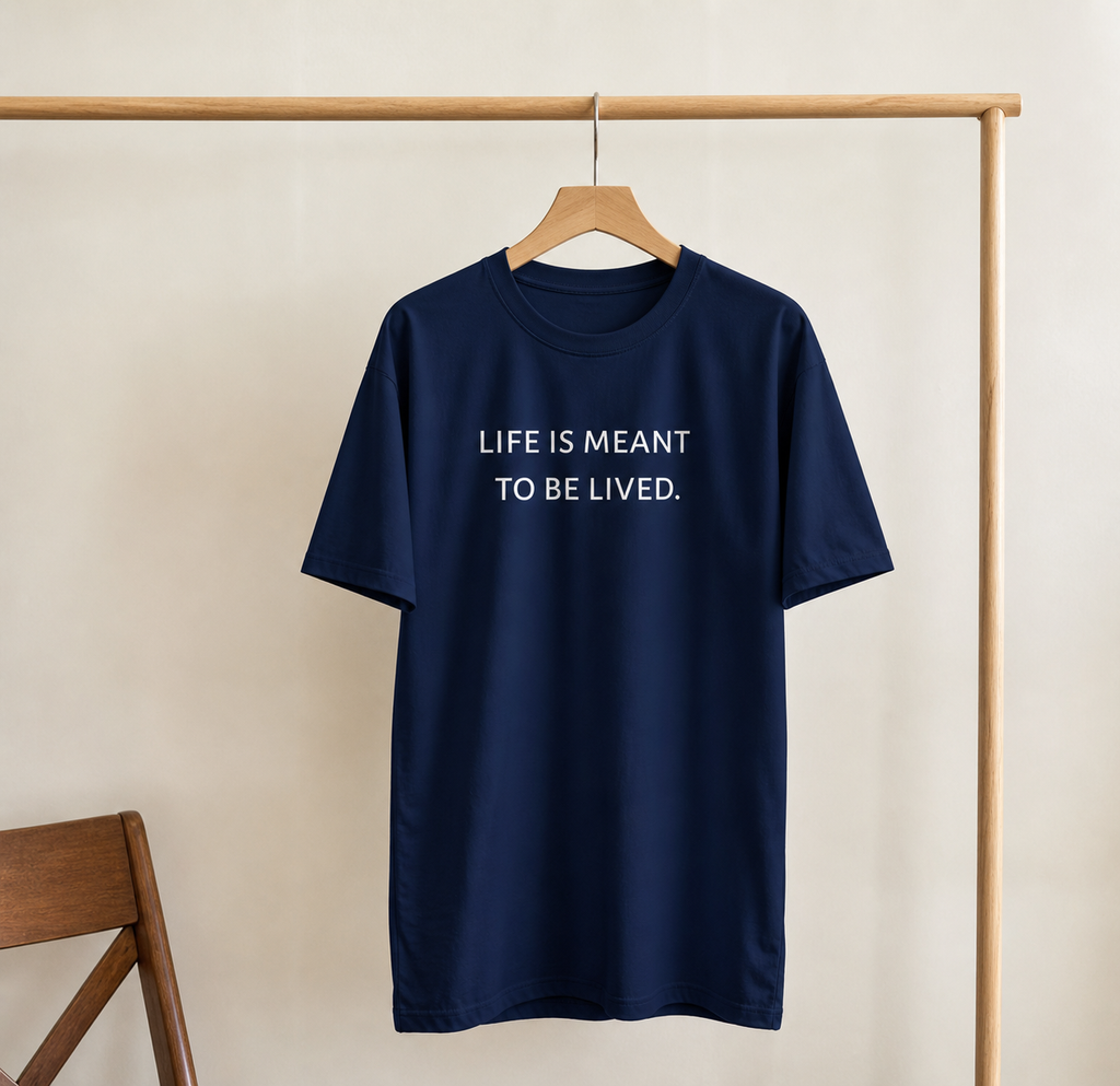 Navy blue t-shirt with 'LIFE IS MEANT TO BE LIVED.' text on a wooden hanger against a beige wall.