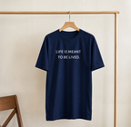Navy blue t-shirt with 'LIFE IS MEANT TO BE LIVED.' text on a wooden hanger against a beige wall.