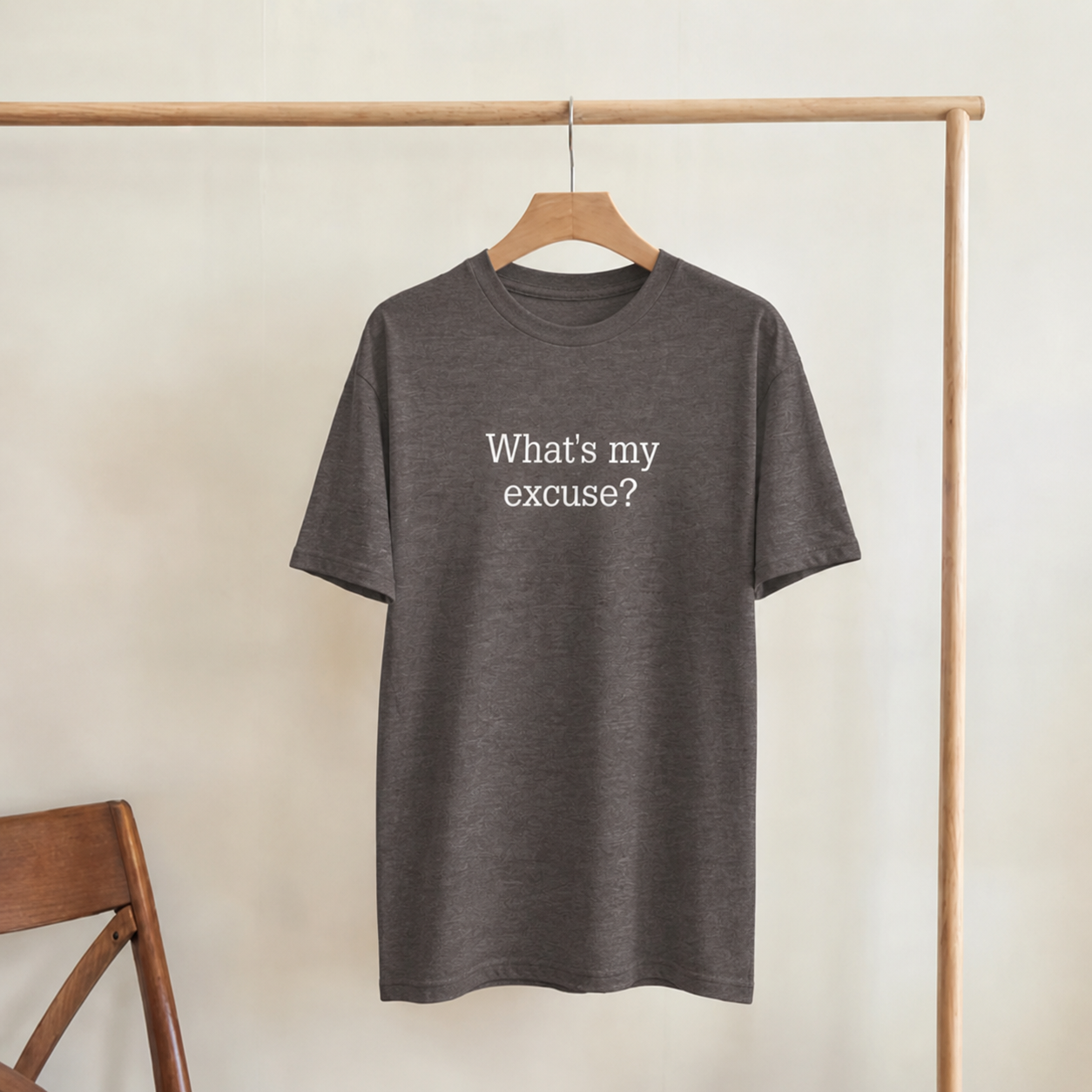 Gray t-shirt with 'What's my excuse?' text on a wooden hanger against a beige wall.
