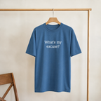 Blue t-shirt with 'What's my excuse?' text on a wooden hanger against a beige wall.